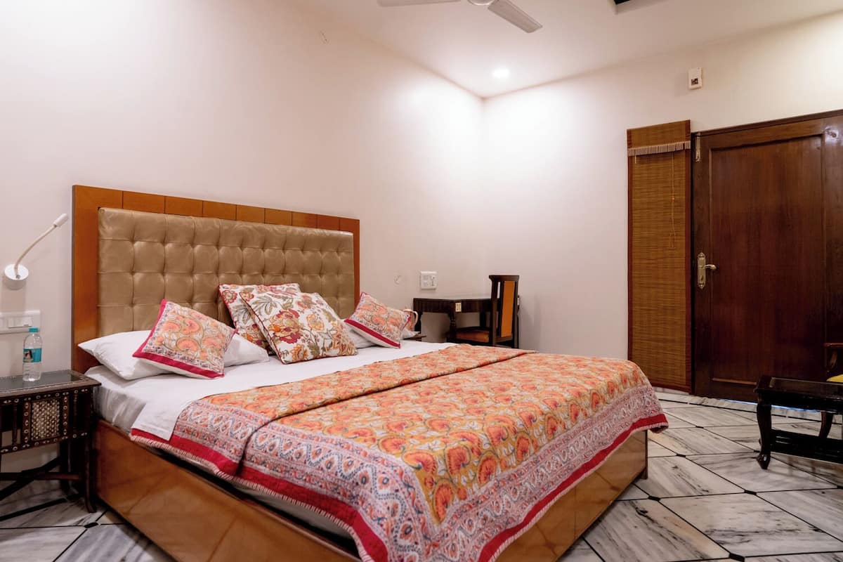 A bedroom with a large bed, a wooden headboard, a nightstand, a desk, and a wardrobe.