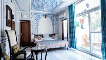 Una habitación con cama, una silla, una mesita pequeña y un ventanal con cortinas.