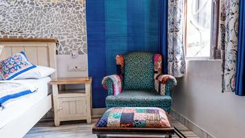 Un dormitorio con cama, mesita de noche, sillón con colcha y ventana con cortinas.