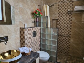 A bathroom with a gold sink, white toilet, shower with glass panels, and a decorative vase with flowers. - All Seasons Heritage Homestay (Jaipur)