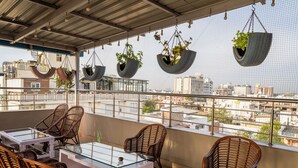 Terraza en la azotea con mobiliario de mimbre, macetas colgantes y vistas a la ciudad.