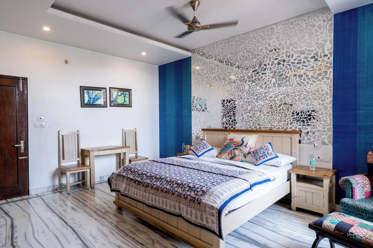A bedroom with a bed, two chairs, a desk, a nightstand, and a decorative wall.