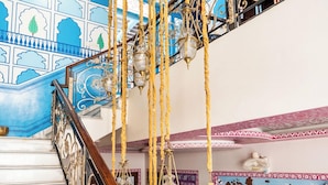 Una imponente escalera con barandillas ornamentadas y lámparas colgantes, que conduce a un balcón con techo decorativo.