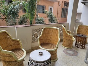 A balcony with wicker chairs and a small table, overlooking a building and greenery. - All Seasons Heritage Homestay (Jaipur)