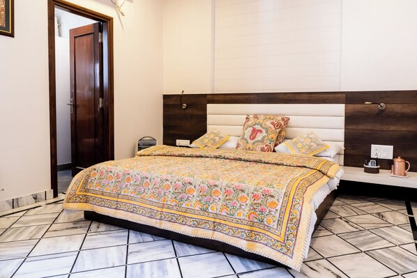 A bedroom with a large bed, a wooden headboard, multiple pillows, a bedside table with a lamp, and a nightstand. - All Seasons Heritage Homestay (Jaipur)
