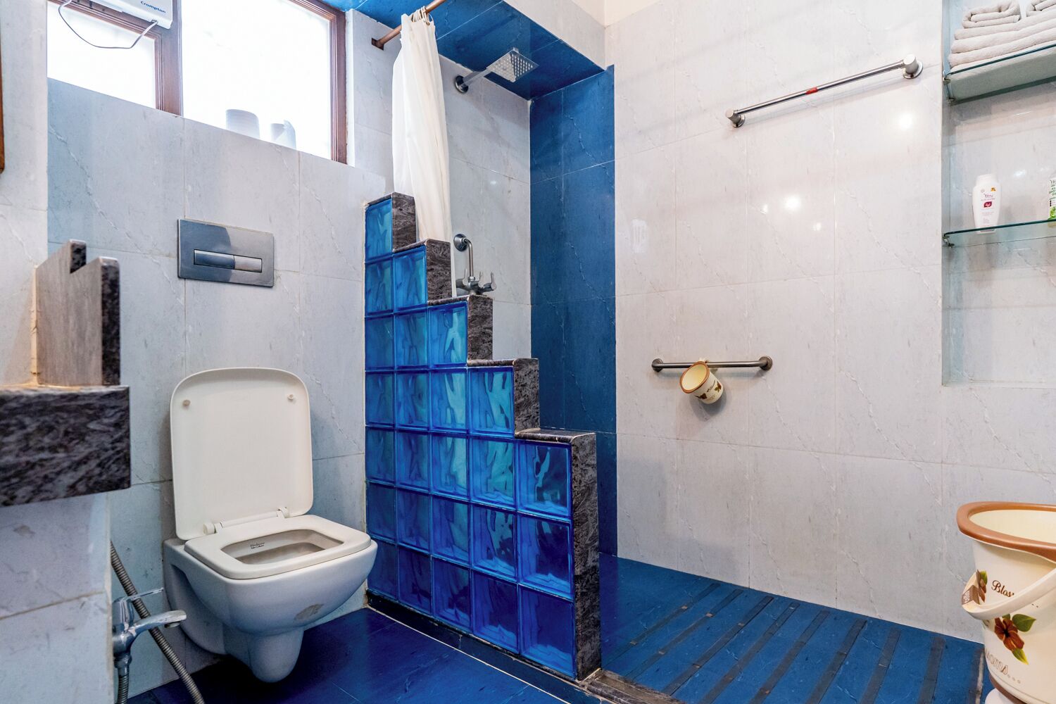 A bathroom with a toilet, a shower with blue tiles, and a handrail.