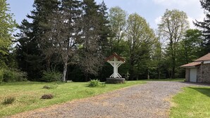 Een grindpad leidt naar een witte pergola met een rood dak, omringd door weelderige begroeiing en bomen.