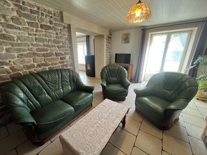 A living room with a stone wall, a green leather sofa, a matching armchair, a wooden coffee table, and a fireplace.