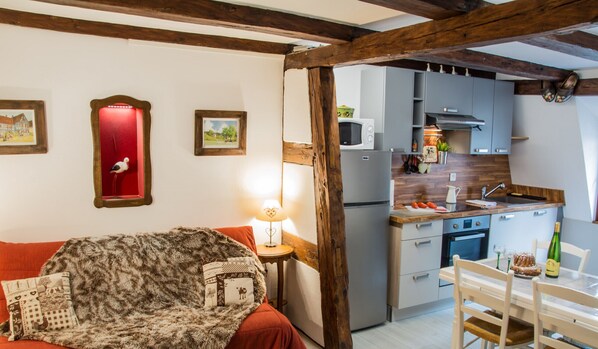 A cozy room with a bed, a lamp, a red mirror, and a kitchen with cabinets and a microwave.