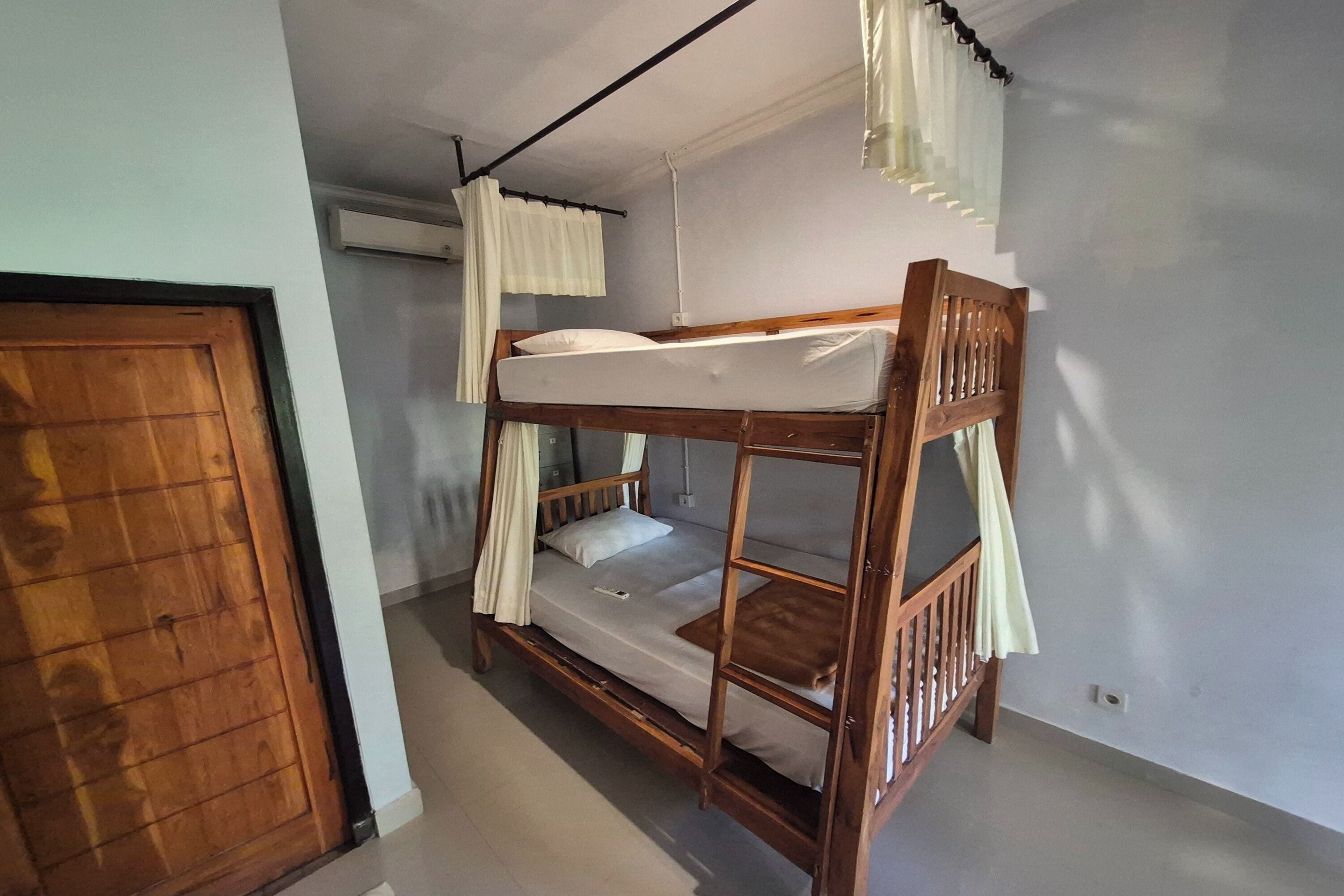 A bunk bed with a wooden frame, white bedding, and a curtain.