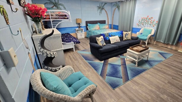 A cozy living room with a sofa, chairs, a cat tree, and a bed with a blue and white patterned bedspread.