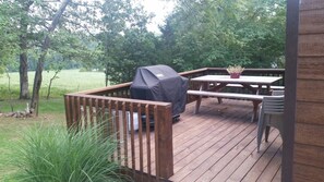 Eine Holzterrasse mit Grill, Picknicktisch und Stühlen.