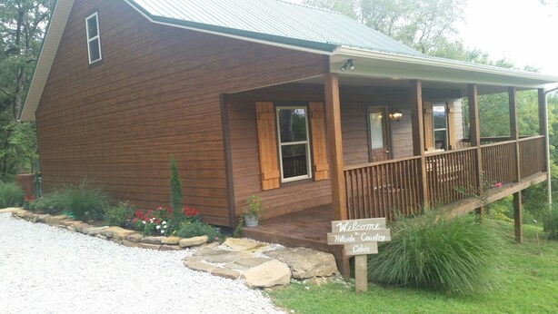 A wooden cabin with a porch, a welcome sign, and a gravel driveway.