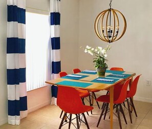 Een eetgedeelte met een tafel voor vier personen, omringd door rode stoelen, een kroonluchter en een potplant.
