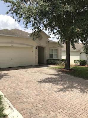 A single-story house with a garage numbered 207, a brick driveway, and a well-maintained lawn.