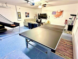 Une table de ping-pong dans une pièce équipée d’un ventilateur de plafond, d’un tél éviseur et décorée d’un drapeau américain.