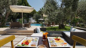 An outdoor dining area with a pool view, wicker furniture, and a table set with food and drinks. - ADELLA GARDEN MARİNA HOTEL (Kusadasi)