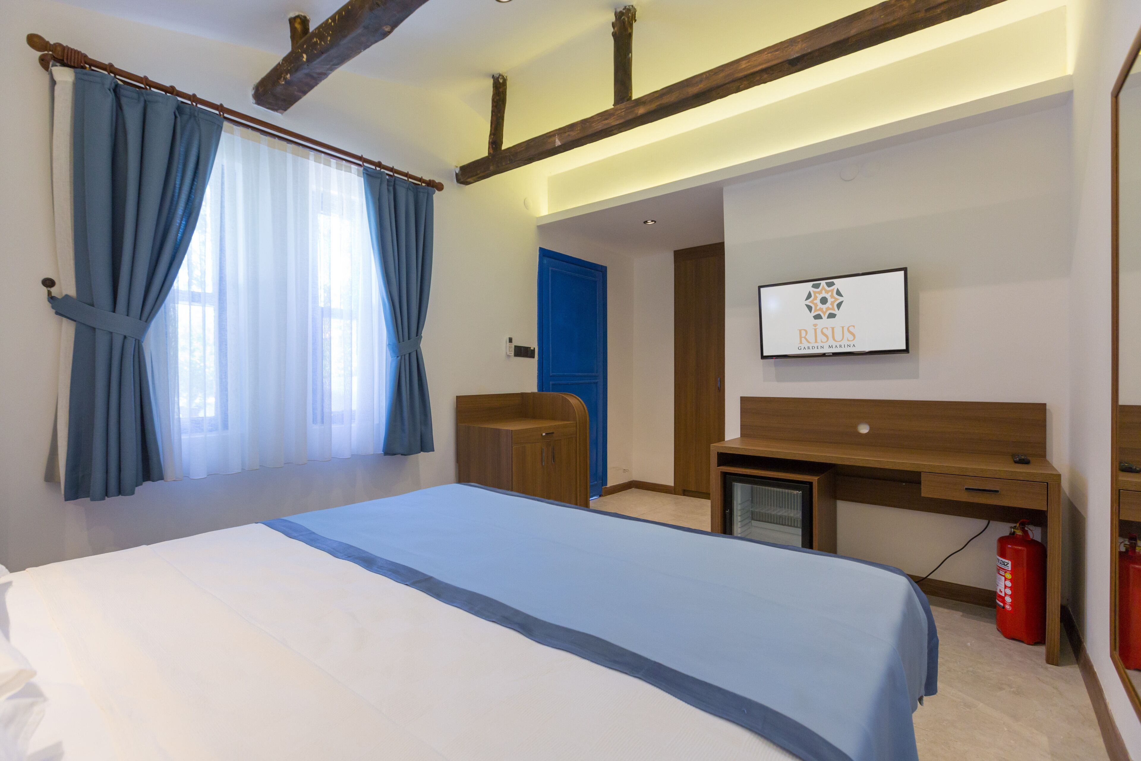 Una habitación de hotel con una cama, un escritorio, una silla, un televisor y una puerta azul.
