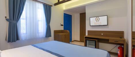 Una habitación de hotel con una cama, un escritorio, una silla, un televisor y una puerta azul.