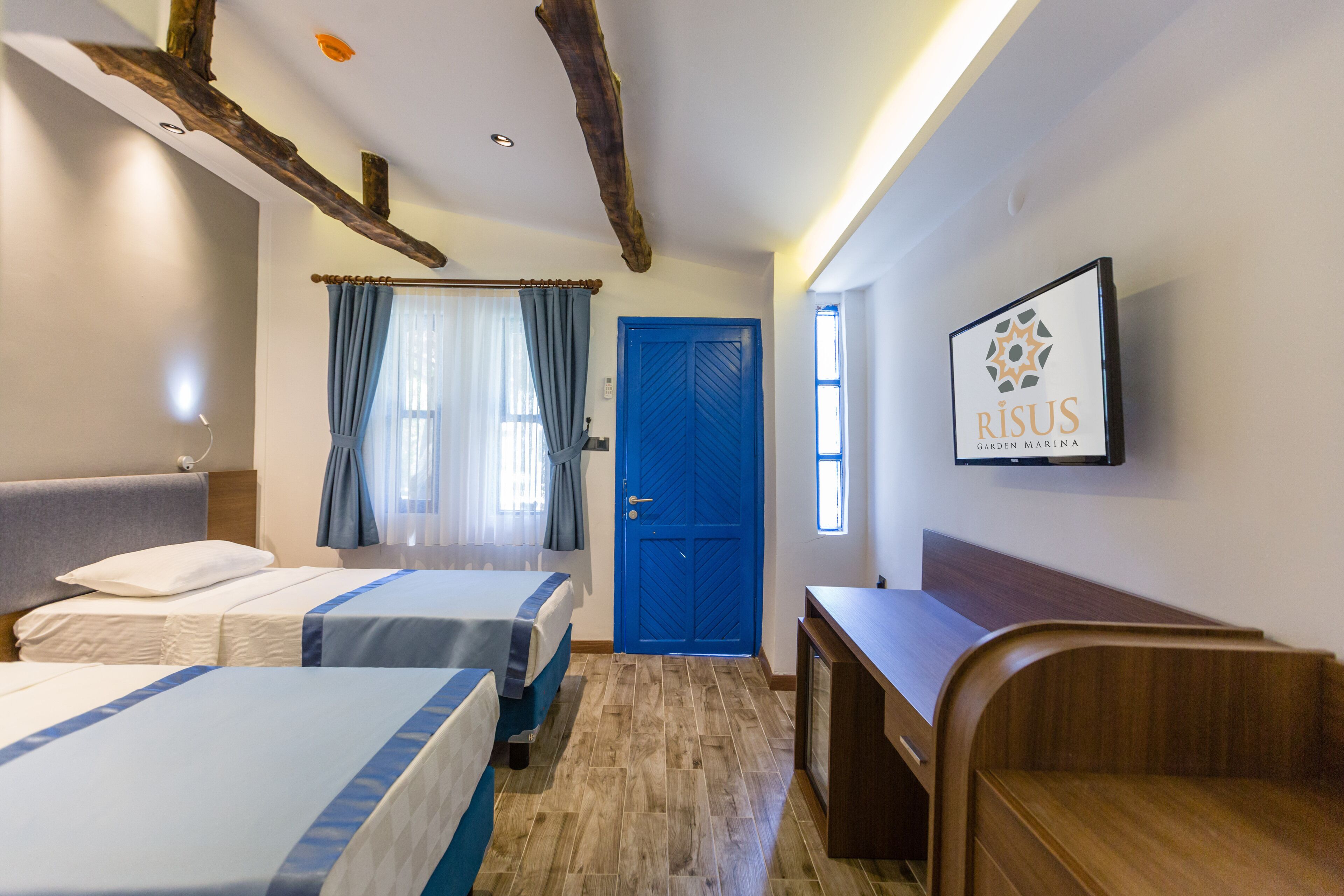 A hotel room with two beds, a blue door, a wooden desk, and a mounted sign.
