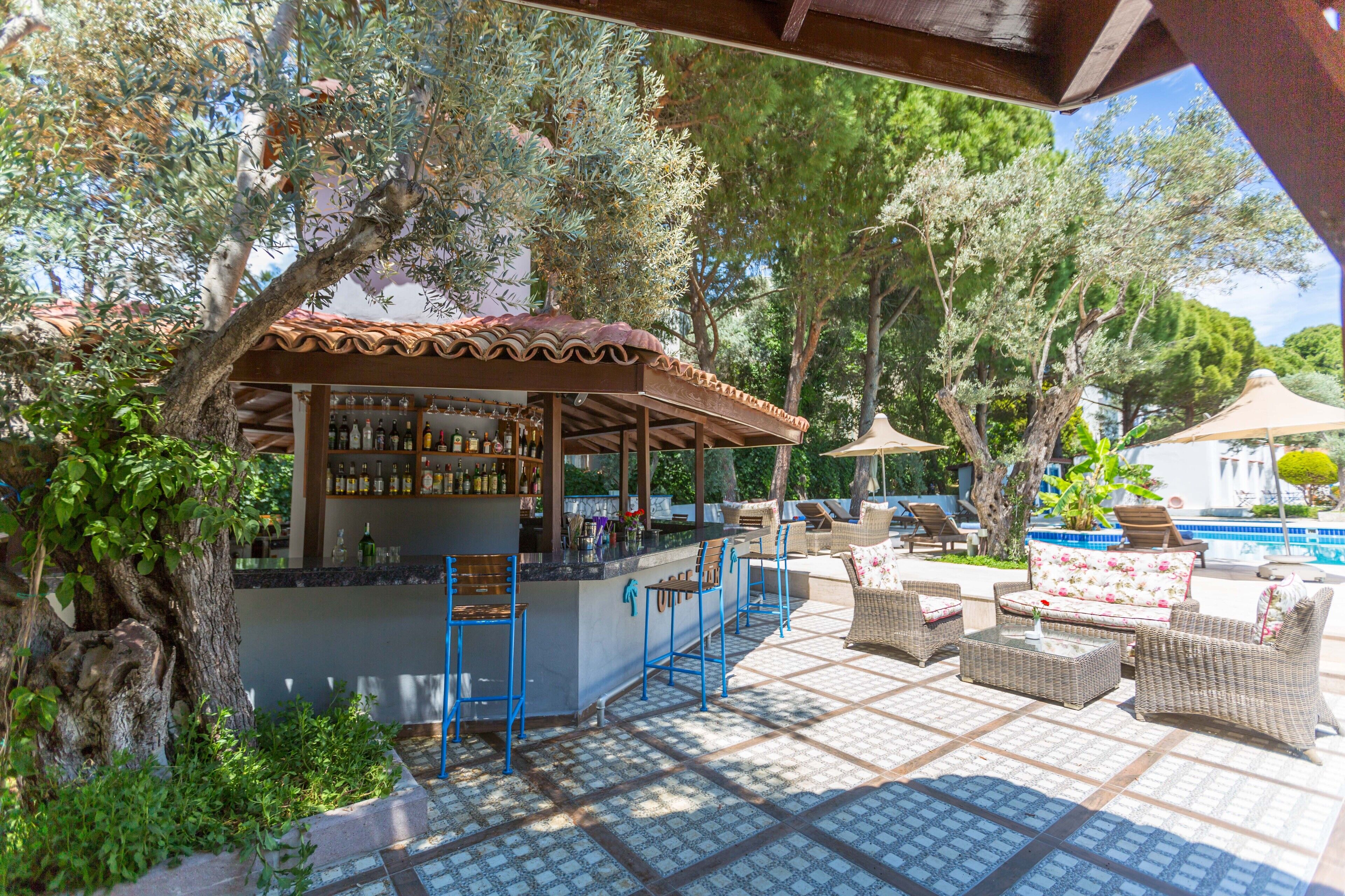 An outdoor bar area with a tiled floor, bar stools, and a poolside seating area with wicker furniture.