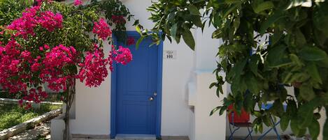 Un bâtiment avec une porte bleue, un panneau indiquant le numéro de la rue, et une chaise rouge devant l’entrée.