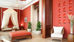 A room with a bed, a sitting area with a chair, a sofa, and a canopy bed. There are potted plants and a wall with a decorative pattern. - Maritim Jolie Ville Resort & Casino (SHARM EL SHEIK)