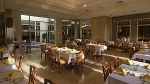 A spacious dining area with multiple tables and chairs, large windows allowing natural light, and a view of the cityscape. - Maritim Jolie Ville Resort & Casino (SHARM EL SHEIK)