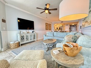 A living room with a television, a ceiling fan, a sofa, a coffee table, and a dining area in the background.