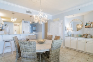 A dining area with a round table, wicker chairs, a central bowl, and a chandelier.