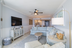 A living room with a sectional sofa, a coffee table, a TV, and a ceiling fan.