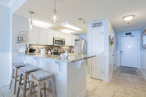 A modern kitchen with white cabinetry, a central island with stools, a microwave, and a refrigerator.