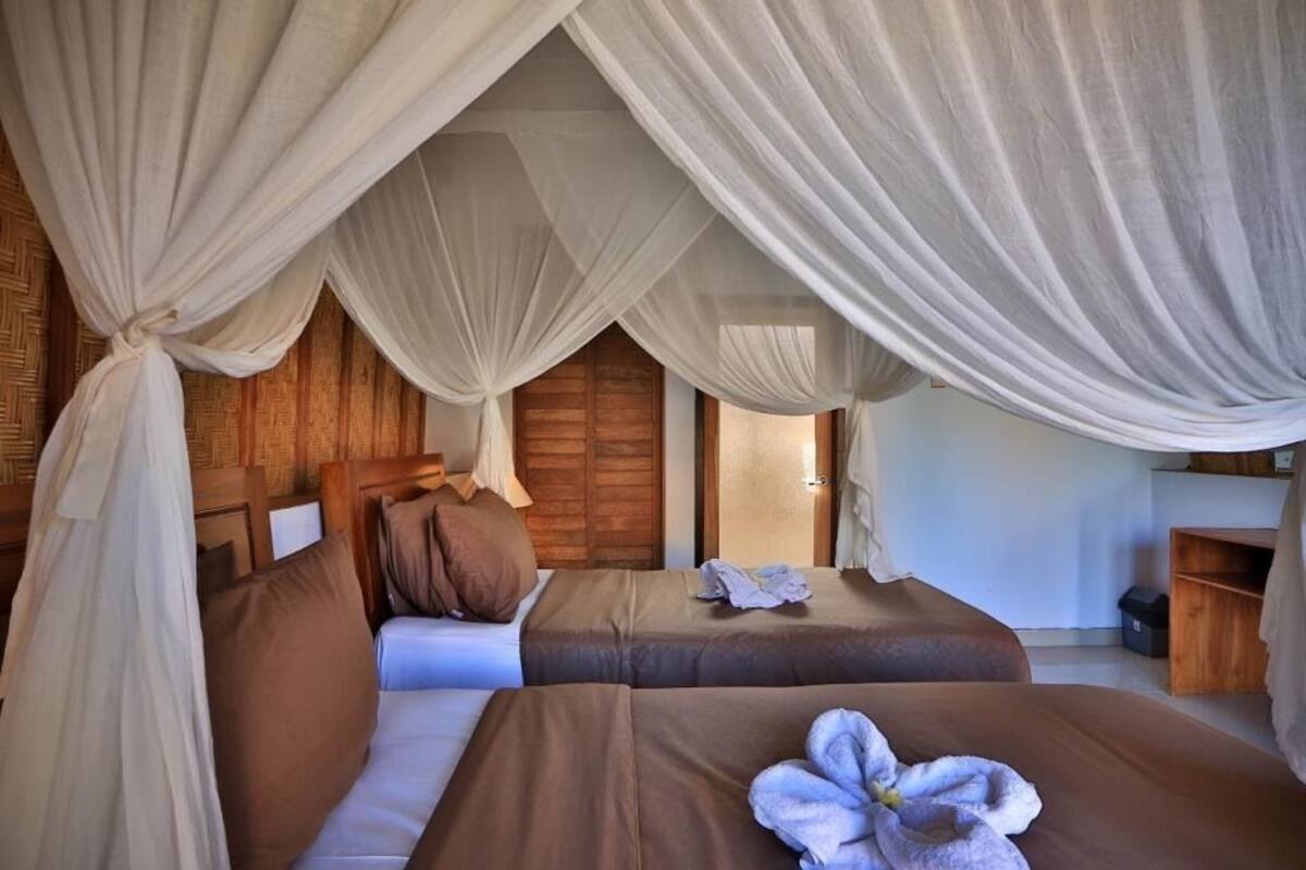 A room with two beds, each with a brown bedspread and pillows, and a canopy bed with white drapes.