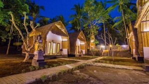 Un resort con cottage a tetto di paglia, un vialetto lastricato e palme.