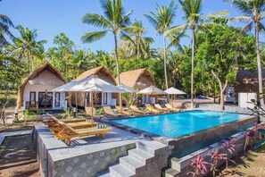 A pool area with lounge chairs and thatched-roof huts, surrounded by palm trees. - Bintang Bungalow (Penida Island)