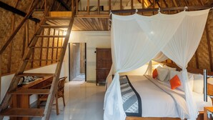 Una stanza con soffitto alto, una scala in legno che conduce a una zona mansardata, un letto a baldacchino e una scrivania con una sedia.