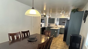 Un coin repas avec une table et des chaises en bois, un luminaire suspendu et une cuisine en arrière-plan.
