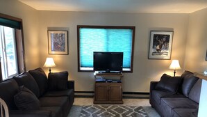 A living room with two dark brown leather sofas, a wooden entertainment center with a flat-screen TV, and a patterned rug. - Ketchikan Northern Retreat - 3 Bedroom Apartment on Large Private Lot (Ketchikan)