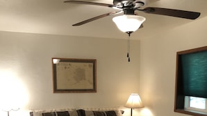 A bedroom with a bed, a ceiling fan, a wall-mounted lamp, a framed map, and a window with a blind. - Ketchikan Northern Retreat - 3 Bedroom Apartment on Large Private Lot (Ketchikan)