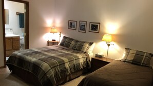 A bedroom with two beds, a nightstand with lamps, a mirror, and a small table with a towel. - Ketchikan Northern Retreat - 3 Bedroom Apartment on Large Private Lot (Ketchikan)
