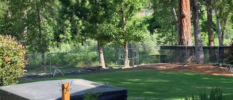 A well-maintained outdoor area with a large tree, a fenced play area, and a small building with a sign.