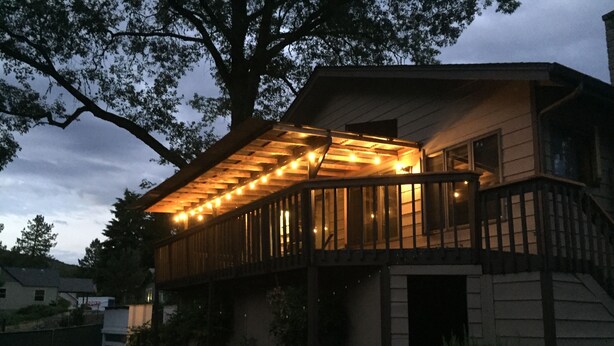 A wooden deck with string lights, a stone pathway, and a large tree.
