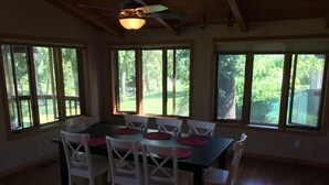 A dining area with a table and chairs, large windows, and a ceiling fan.