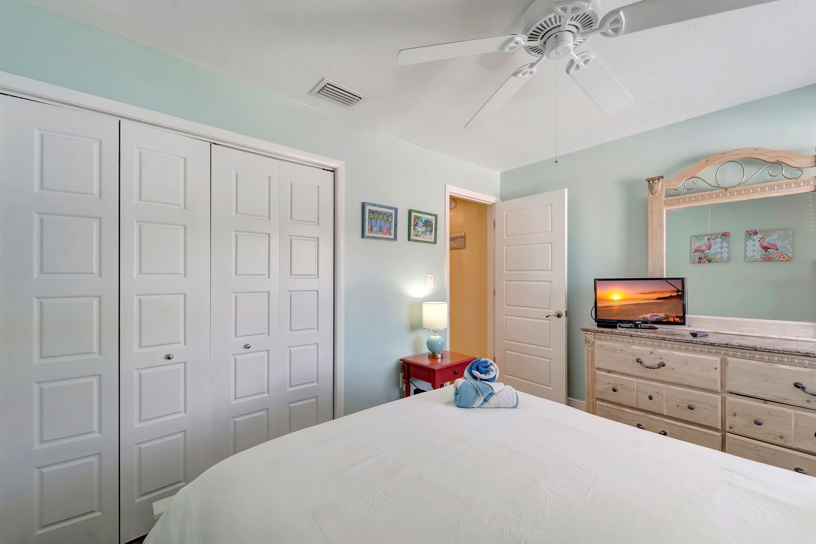 Un dormitorio con cama, cómoda, televisor y ventilador de techo.