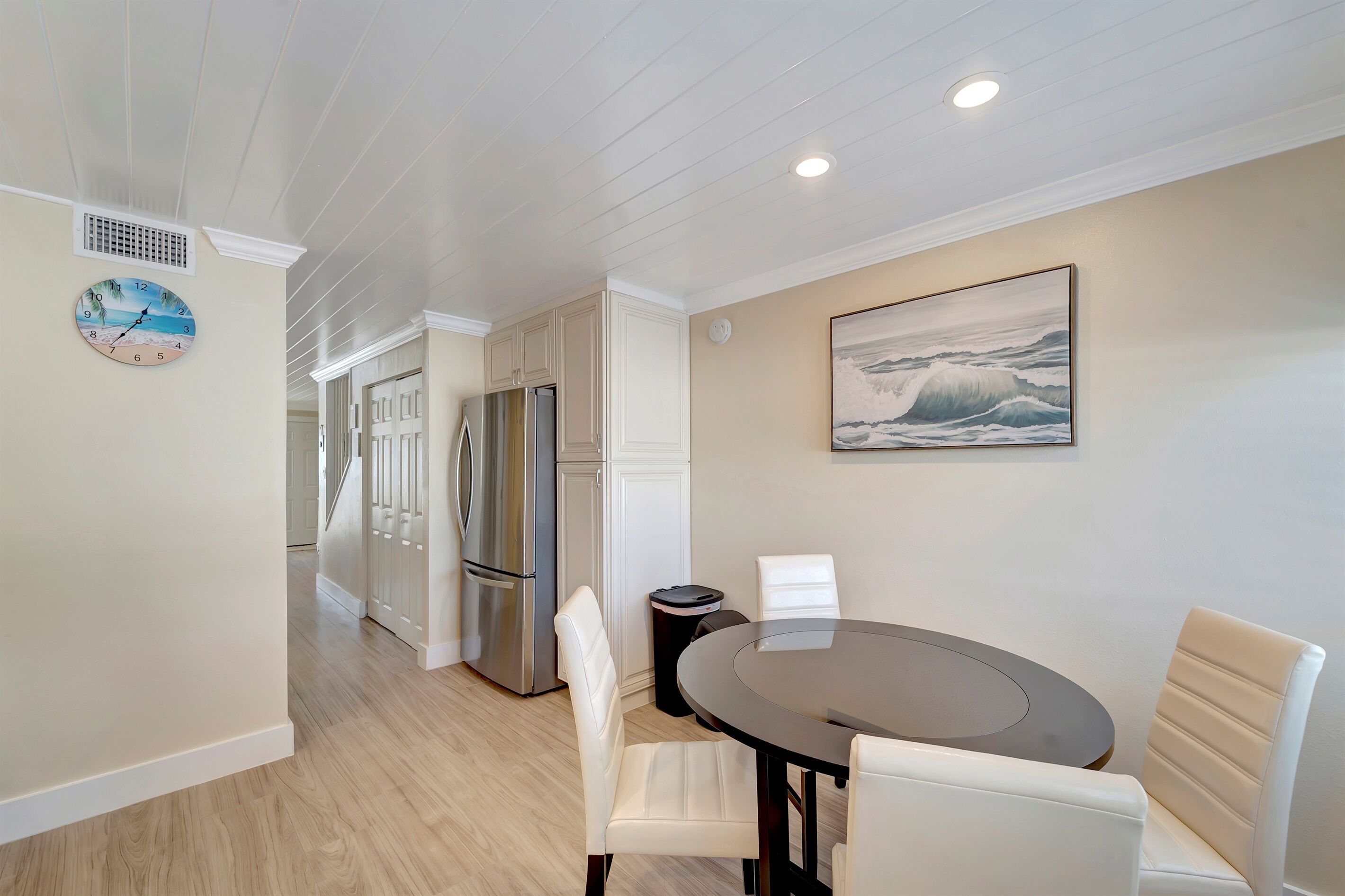 A modern kitchen with white cabinetry, a stainless steel refrigerator, and a round dining table with white chairs.