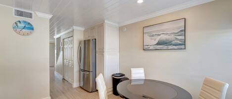 A modern kitchen with white cabinetry, a stainless steel refrigerator, and a round dining table with white chairs.