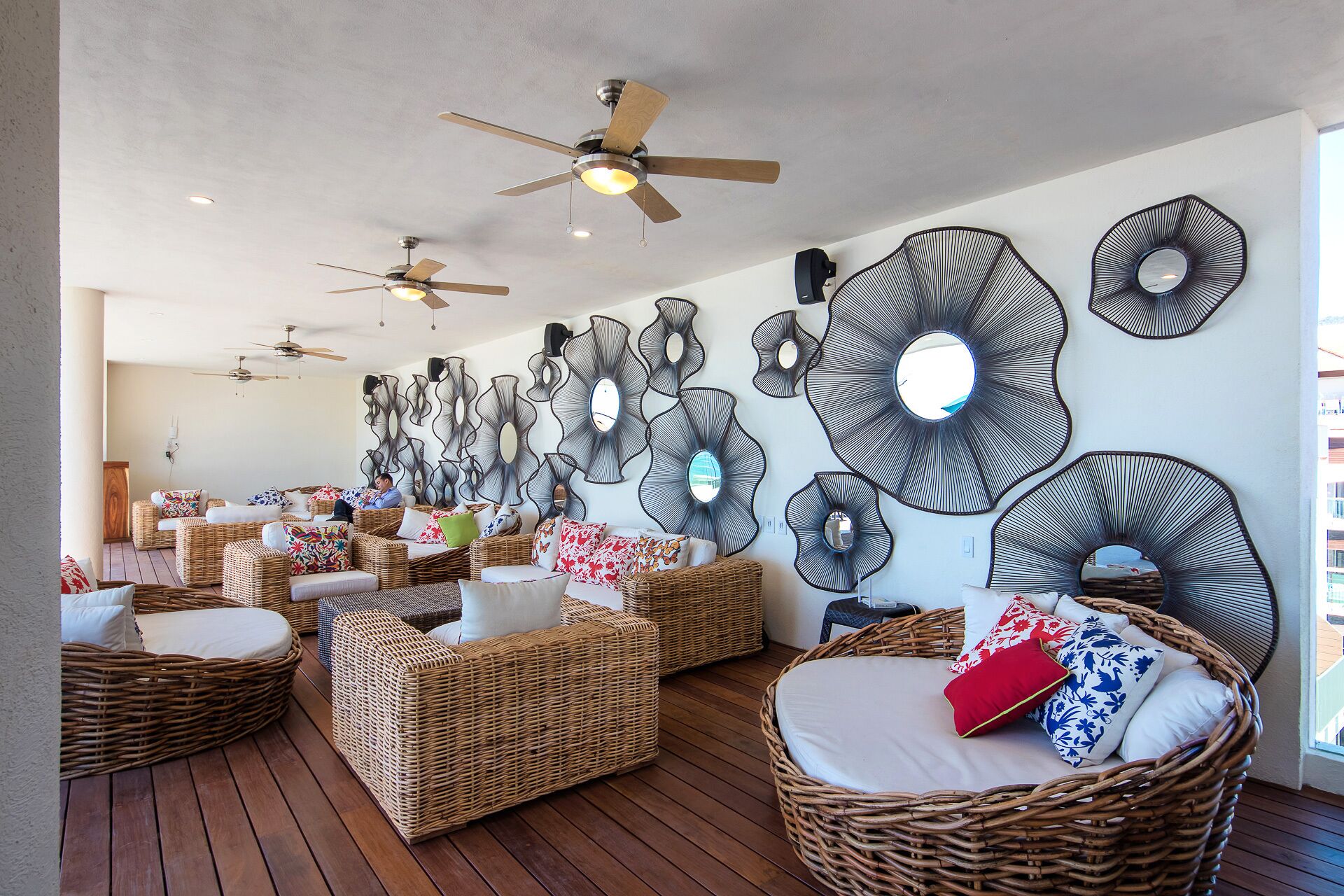 A spacious room with wicker furniture, ceiling fans, and decorative wall mirrors.