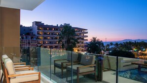 Ein Balkon mit Glasgeländern, Holzstühlen und einem Poolbereich.