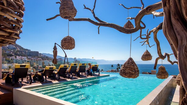 Ein Poolbereich mit Liegestühlen, einem klaren blauen Pool und Blick auf das Meer und ferne Berge.