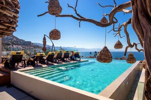 A poolside area with lounge chairs, a clear blue pool, and a view of the sea and distant mountains. - Ocean view apartment Zona Romantica with amazing rooftop pool and terrace! (Puerto Vallarta)